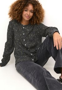 Chemise à manches longues à fleurs sombres avec boutons blancs et coupe décontractée, associée à un pantalon large gris foncé.