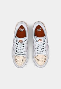 Nike SB Force 58 superge se ponašajo z mešanico svetlo sive, bež in nežno rožnate zamšene kože, z perforiranimi detajli in rdeče-oranžnim logotipom.