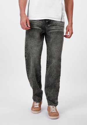 Grey denim jeans with a faded finish, straight fit, and subtle creasing. Paired with brown suede sneakers and a white shirt.