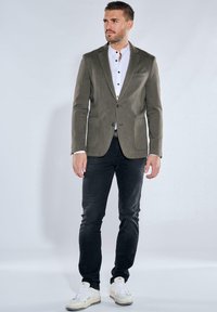 Grau strukturierte Blazer über einem weißen Hemd mit Knopfdesign, kombiniert mit schwarzen Slim-Fit-Jeans und weißen Sneakers.