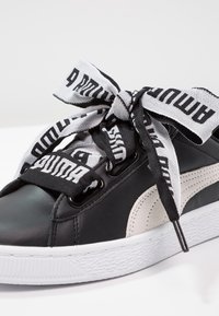 Černé kožené tenisky s texturovanou bílou gumovou podrážkou, s velkým černobílým logem zavázaným na mašli.