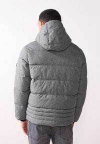 Giacca imbottita grigia con cappuccio, caratterizzata da una trapuntatura orizzontale e un tessuto testurizzato, abbinata a jeans grigi scuri.