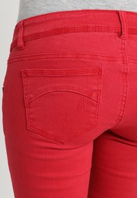 Vaqueros de mezclilla rojos con corte ajustado, dos bolsillos traseros y detalles de costura texturizada en los bolsillos y la tela.