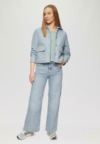 Veste courte bleu clair avec deux poches avant, fermeture à boutons et texture douce. Associée à un jean large bleu clair et des baskets argentées.