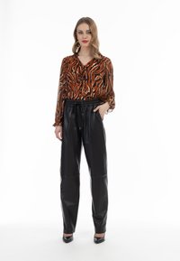 Orange och svart randig blus med långa ärmar och slipskrage, ihop med höga svarta läderjoggingbyxor och svarta klackar.