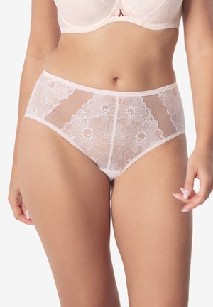 Kobieta w półprzezroczystych białych koronkowych majtkach z wysokim stanem i pasującym biustonoszu, stojąca na białym tle.