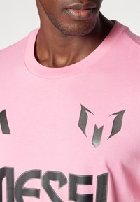 Pink cotton t-shirt featuring bold black graphic text and logo, round neck, and short sleeves; smooth texture with minimal seams.