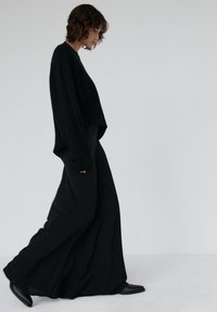 Czarny, oversize'owy sweter z opuszczonymi ramionami, zestawiony z długą czarną spódnicą. Oba elementy odzieży mają miękką fakturę i płynną sylwetkę.