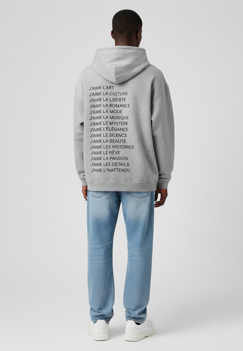 Felpa grigia con testo nero sul retro che recita "J'aime" seguito da varie frasi. Abbinata a un paio di pantaloni in denim azzurro chiaro e sneakers bianche.