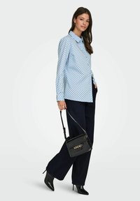 Chemise bleu clair à pois noirs, à manches longues, avec un col. Associée à un pantalon large noir et à un sac à main noir texturé.