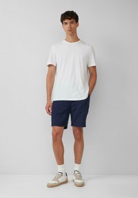 T-shirt en coton blanc associé à un short bleu marine, des chaussettes blanches et des baskets beige. Look décontracté avec un design simple et peu de détails.