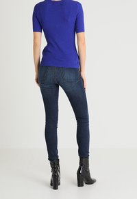 Royal blue ribbed short-sleeve top paired with dark denim jeans, featuring a fitted silhouette and ankle-height black heeled boots.