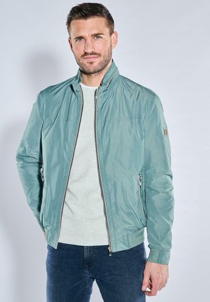 Light green bomber jacket with a high collar, zip closure, side pockets, and ribbed cuffs. Worn over a light gray sweater.
