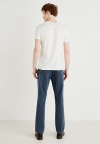 T-shirt de algodão branca com um corte clássico em gola redonda, combinada com jeans azuis com bolsos traseiros e corte reto. Sapatos pretos.
