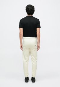 Juoda trumpomis rankovėmis marškinėliai, derinami su šviesiai smėlio spalvos laisvalaikio kelnėmis su elastinga juosmens juosta ir galine kišenė su logotipu. Juodi batai.