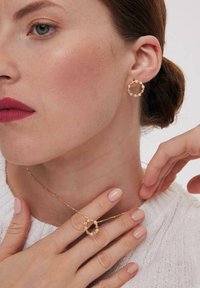 Złoty zestaw biżuterii składający się z okrągłego naszyjnika z drobnymi perłami oraz pasujących kolczyków w formie obręczy. Modelka ma na sobie jasny sweter.