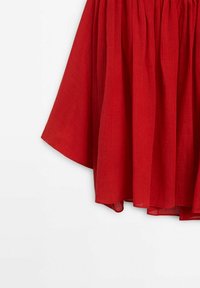 Rød linnednederdel med en samlet talje og flydende kant, der har en glat tekstur og et lagdelt, let design.