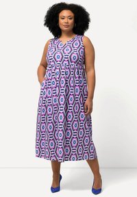 Maxikleid in lila mit geometrischen Mustern, ärmelloses Design, V-Ausschnitt und Taschen, kombiniert mit blauen Absätzen. Weicher Stoff und lockerer Schnitt.