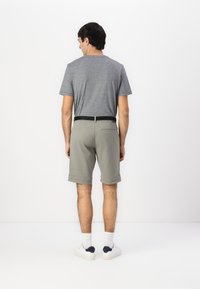 T-shirt gris clair et shorts kaki avec une taille noire ; les shorts ont des ourlets roulés et une poche arrière. Baskets blanches avec des accents marins.