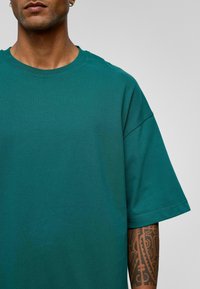Teal katoenen T-shirt met een ronde hals, korte mouwen en een relaxte pasvorm. Gestructureerde stof met zichtbare stikseldetails.