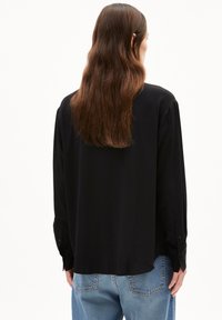 Schwarzes Langarmhemd mit entspannter Passform, ausgestattet mit geknöpften Manschetten und einer glatten Textur, kombiniert mit hellblauen Jeans.