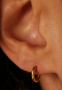 Gouden oorbel in een geperforeerd oor, gladde textuur, ronde vorm, met een gepolijste afwerking die lichtreflecties vangt.