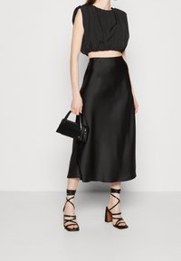 Top court noir avec des épaules froncées, associé à une jupe midi noire en satin élégante. Accessoirisé avec un petit sac à main noir et des sandales à lanières.