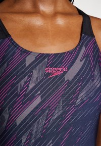 Maillot de bain de course de couleur marine avec des rayures diagonales roses et des motifs en mesh. Il présente un col rond et un logo Speedo rose sur la poitrine.