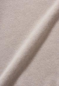 Hellbeiges, gestricktes Gewebe mit weicher, glatter Textur und dezenten Farbnuancen, gefaltet, um Tiefe und Materialdetails zu zeigen.