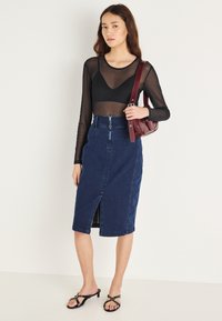 Juodas permatomas ilgomis rankovėmis viršus, tamsiai mėlynos džinsinio audinio pieštuko formos sijonas su priekiu kirpimu, juodos aukštakulnės basutės; bordo kryžminių dirželio rankinė.