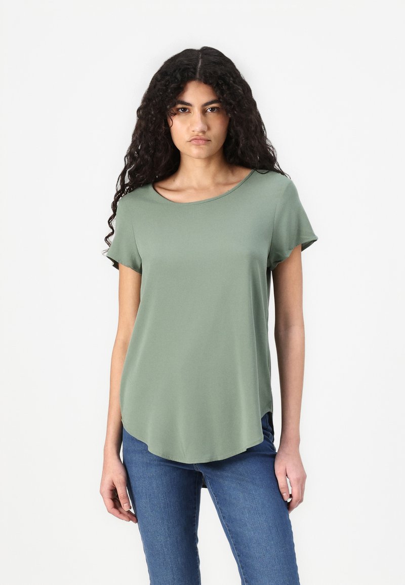 Short-sleeved, scoop-neck t-shirt in muted green, featuring a curved hem and smooth texture, paired with blue jeans.