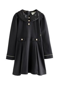Vestito nero a maniche lunghe con colletto Peter Pan lucido, bottoni di perla sulla patta frontale e sulle tasche, gonna plissettata e bordatura bianca sui polsini.