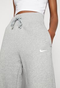 Grå sweatpants med en mjuk textur, elastisk midja, dragsko och en vit Nike-logga på vänster sida.