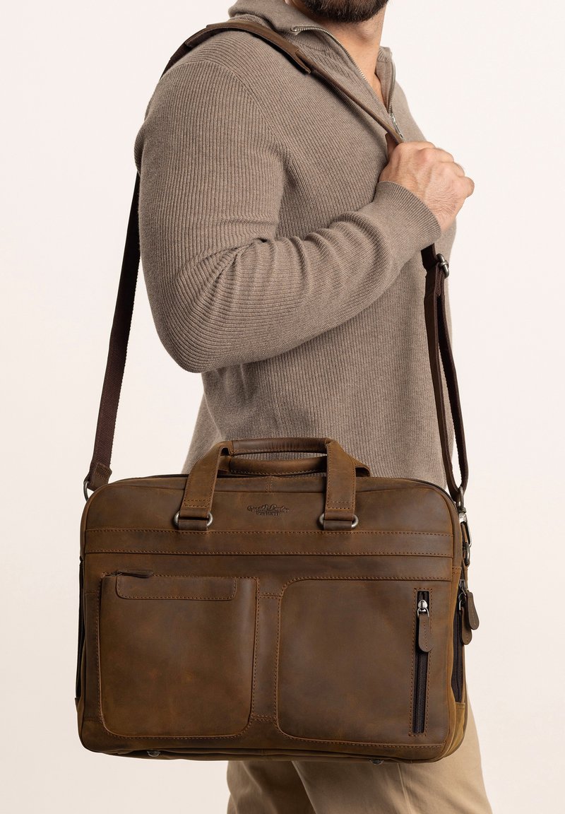 Braune Lederaktentasche mit zwei oberen Griffen und einem abnehmbaren Schultergurt, ausgestattet mit mehreren Reißverschluss- und Steckfächern zur Organisation.