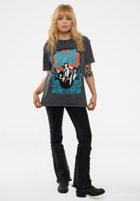 Dark gray graphic t-shirt features a colorful print with figures, surrounded by blue Celtic knot design; paired with black flared jeans and boots.