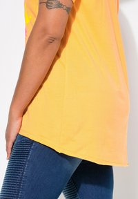 T-shirt jaune à manches courtes avec ourlet droit, associé à un jean en denim bleu texturé avec des détails côtelés sur les jambes.