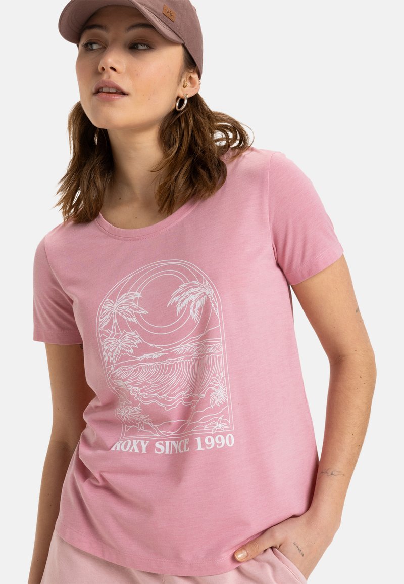 Camiseta de algodón rosa claro con mangas cortas, que presenta un diseño impreso de palmera blanca y ola, y el texto "Roxy Desde 1990" debajo.