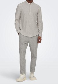 Lichtgrijs shirt met lange mouwen, een henley-halslijn en knoopaccenten, gecombineerd met grijze gestreepte broek en witte chunky sneakers.