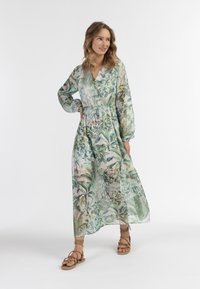Rochie maxi dintr-un material transparent și ușor, cu un imprimeu botanic verde. Dispune de mâneci lungi, talie strânsă și decolteu în V.