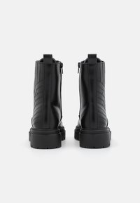 Botas de cuero negras hasta el tobillo con un patrón texturizado en zigzag, cremallera trasera y suelas gruesas para una mejor agarre.