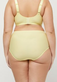 Geel geribbeld beha en high-waisted slips. Zacht materiaal met golvende randen. Verstelbare hardware op de beha-bandjes.