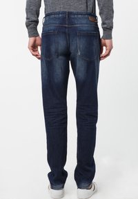 Mörkblå denimjeans med smal passform, med bakfickor och subtila blekningar vid låren. Matchas med en grå långärmad skjorta.