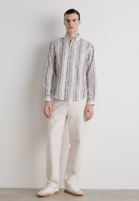 Camisa de botones con rayas verticales multicolores, mangas largas, botones blancos y cuello puntiagudo. Combinada con pantalones color crema y zapatillas blancas.