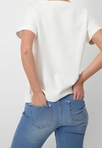 Valkoinen lyhythihainen paita, jossa on pyöreä kaula-aukko, yhdistettynä vaaleansinisiin farkkuihin, joissa on tiukka leikkaus ja näkyvät takataskut.