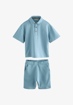 Vaaleansininen lyhythihainen polo, jossa on kolme nappia, yhdistettynä yhteensopiviin sortseihin, joissa on joustava vyötärö ja taskut. Pehmeä kangas.