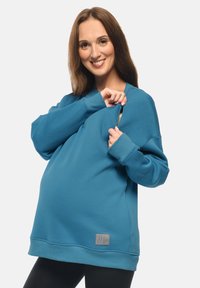 Felpa azzurra chiara con vestibilità morbida, realizzata in materiale morbido. Presenta una cerniera per un accesso facile, polsini a costine e un'etichetta con logo sul fondo.