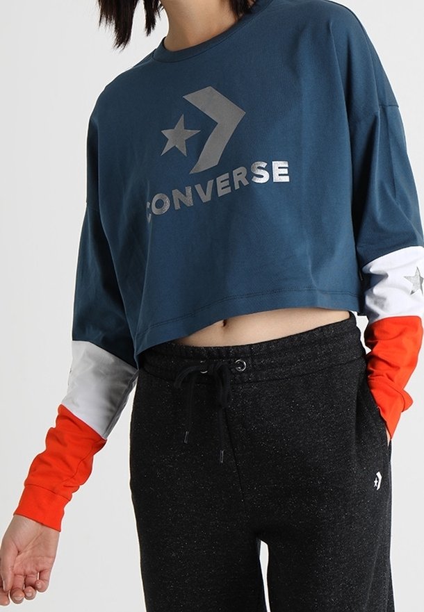 Krátká modrá mikina se stříbrným logem "Converse", hvězdou a designem chevron, s dlouhými rukávy v oranžové a bílé barvě, doplněná černými tepláky.