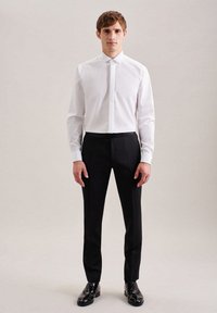Camicia bianca a maniche lunghe con colletto a punta, abbinata a pantaloni eleganti neri; scarpe nere lucide completano l'outfit formale.