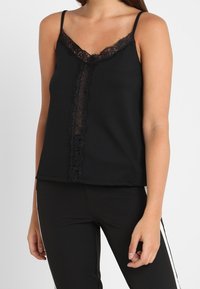 Camisole noire avec bordure en dentelle le long du décolleté et au centre. Fabriquée en tissu doux avec des bretelles fines ajustables.