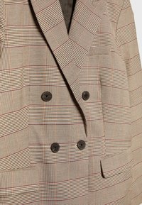 Blazer doppiopetto beige a quadri con motivo check, quattro bottoni scuri, rever a punta e due tasche frontali.